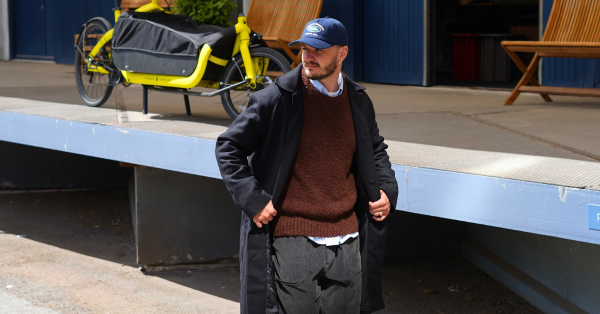 Outfit #037 med sort uldfrakke, brun strik over blå skjorte, mørke fløjlsbukser og navy cap
